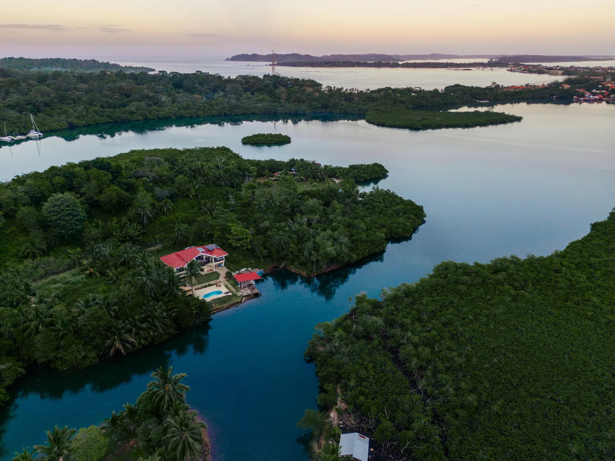 Coconut Coast Villa from the air — the house, pool, palapa and private dock on the canal, with Almirante Bay and Bocas Town beyond, Bocas del Toro, Panama